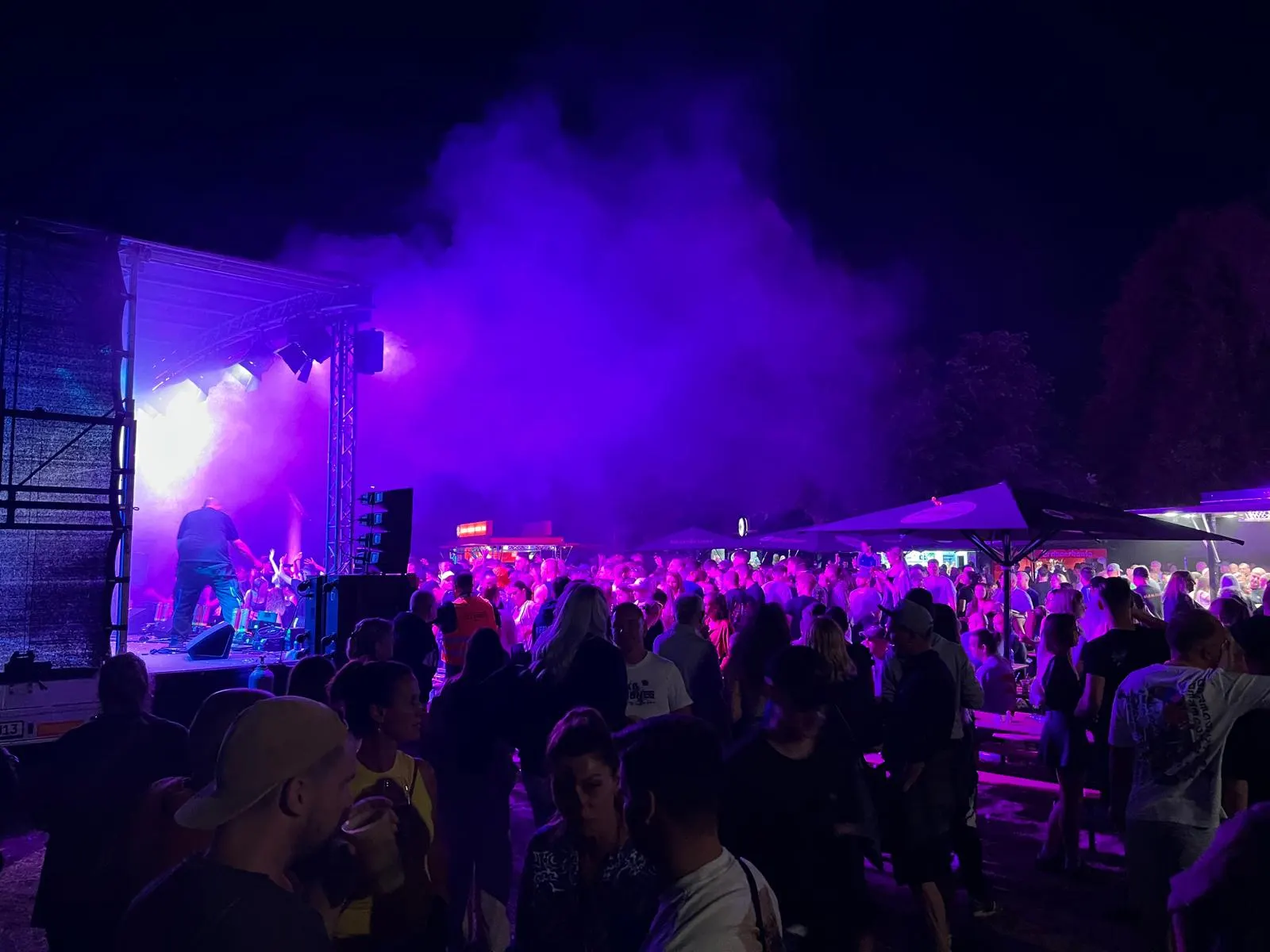 Konzert bei Nacht: Bühne in violettem Licht, davor ein dicht gedrängtes Publikum