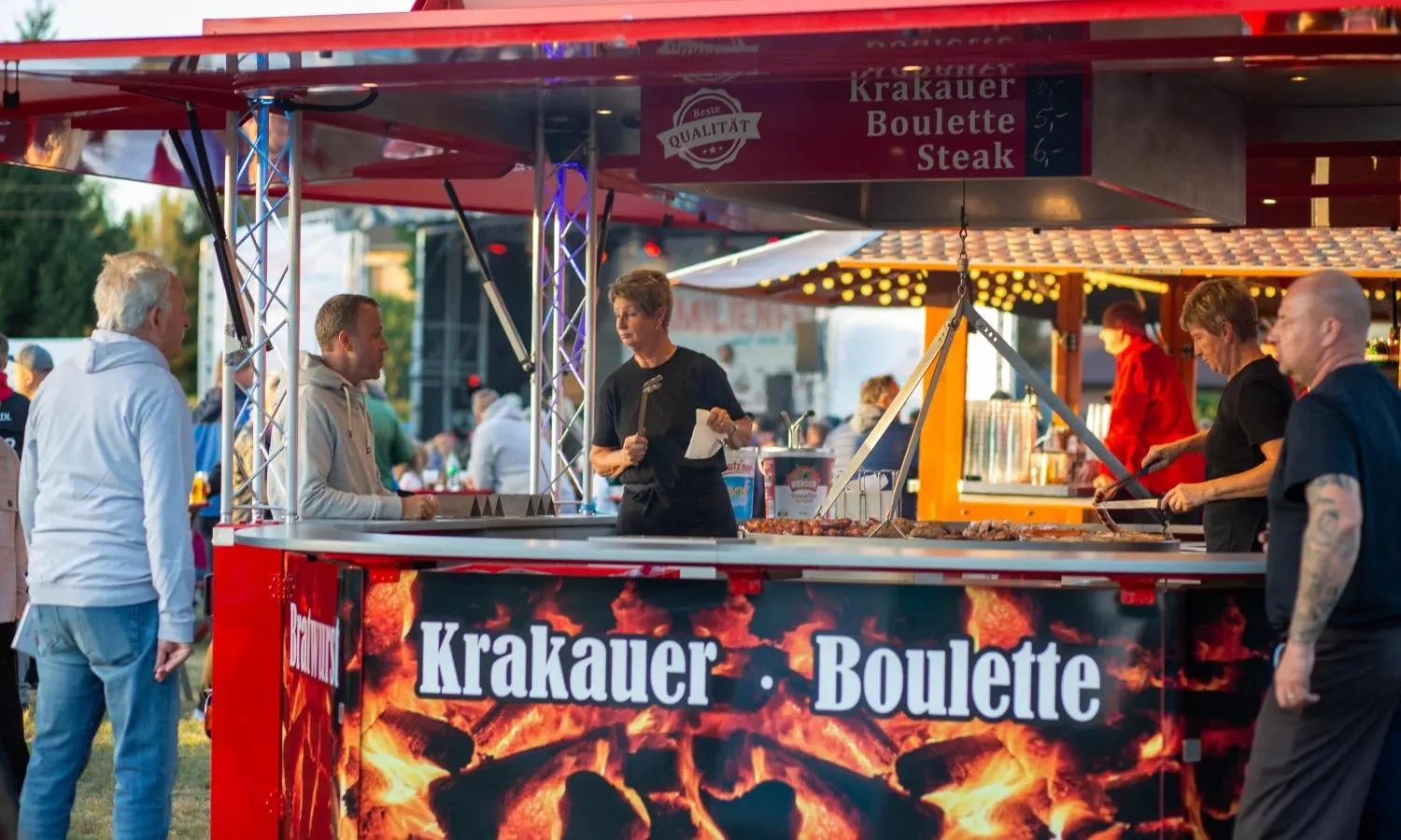 Der rote Grillwagen von Pinkawa Catering am Abend, das Team bereitet an der Theke Krakauer und Bouletten zu